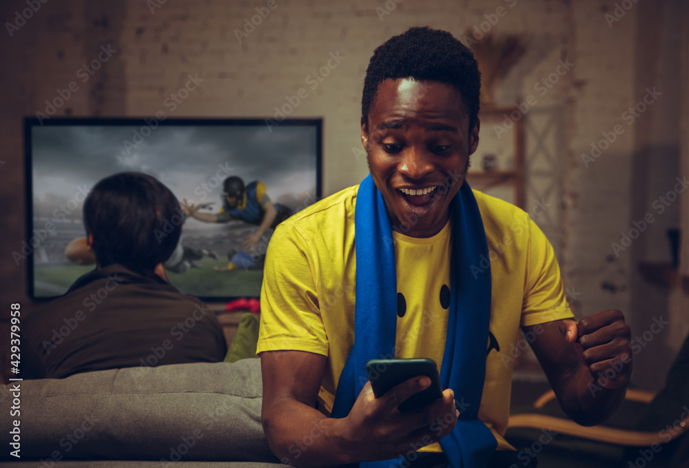 Man with betting application in phone. Group of friends watching TV, sport match together. Emotional fans cheering for favourite team, watching on exciting game.