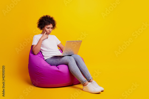 Portrait of woman with laptop computer sit beanbag finger chin ponder look screen isolated on yellow background