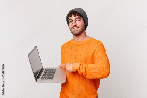 nerd man with computer smiling cheerfully, feeling happy and pointing to the side and upwards, showing object in copy space photo