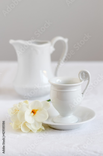 Minimalistic and clean coffee table styling. Elegant white cup of coffee with milk pitcher and blooms of freesia beside.