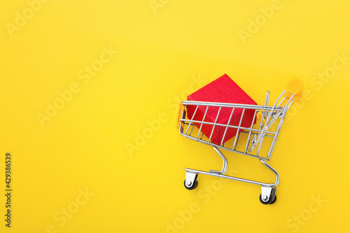 Red box in shopping cart on yellow background, flat lay