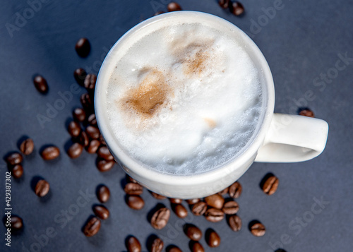 Beautiful latte macchiato with milk foam in a white cup with coffee beans near it. Dark blue background. Cup of coffe with milk. Hot latte or Cappuccino prepared with milk with copy space