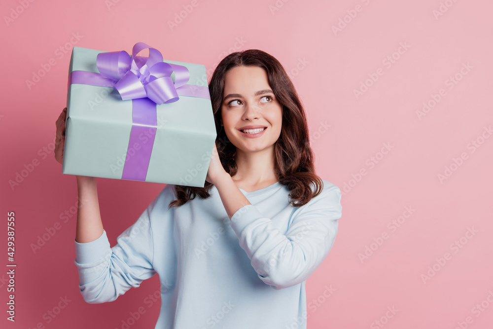 Portrait of a cheerful interested girl holding present box guess look empty space Portrait of a cheerful interested girl holding present box guess look empty space