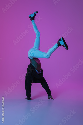 Young stylish man in modern street style outfit isolated on gradient background in neon light. African-american fashionable model in look book, musician performing.