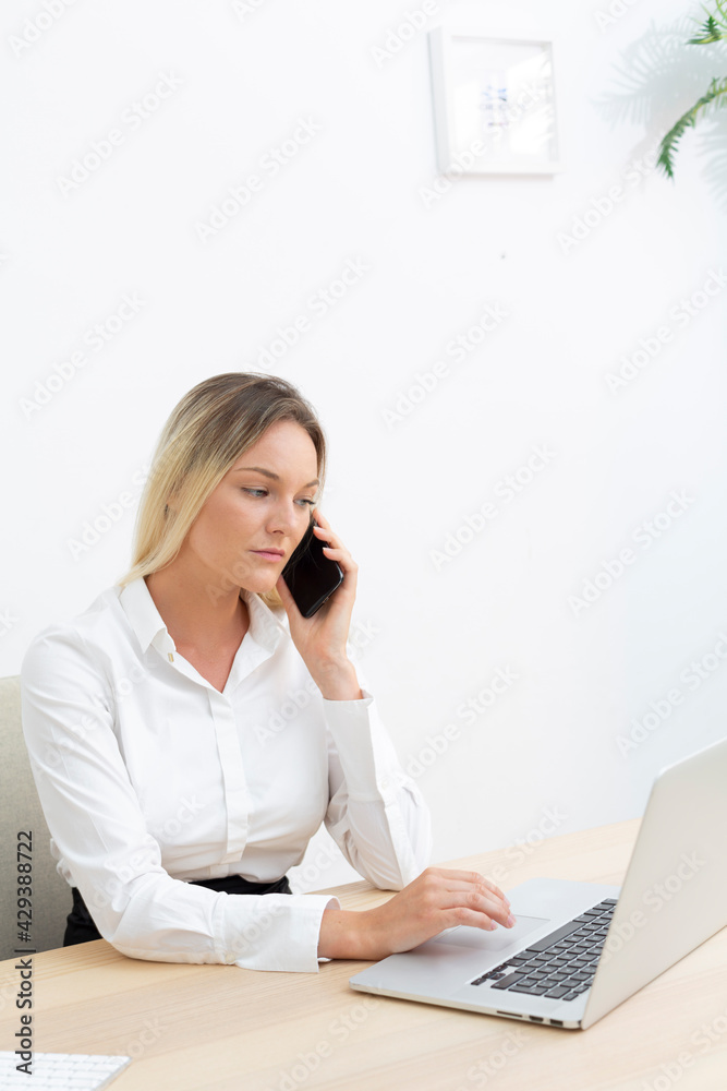 Young attractive businesswoman working in office in front of computer with smartphone. Young attractive businesswoman working in office in front of computer with smartphone.