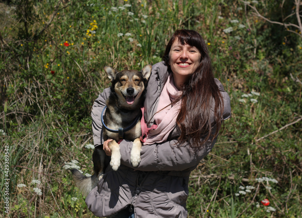Smiling female portrait with smiling dog in her arms, surrounded by nature and spring flowers Smiling female portrait with smiling dog in her arms, surrounded by nature and spring flowers