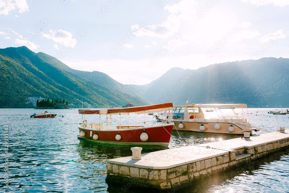 Red and beige pleasure boats on the water at the pier in the town of Perast.