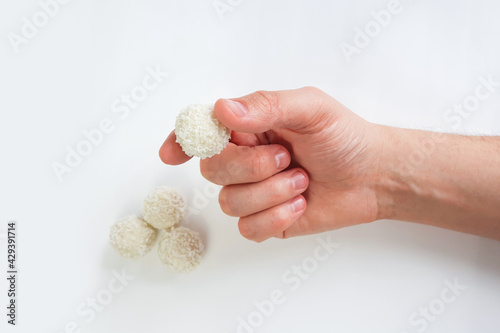 Male hand holds white chocolate candy on white background. Handmade candies, Sweet balls. Isolated background. Selective focus.