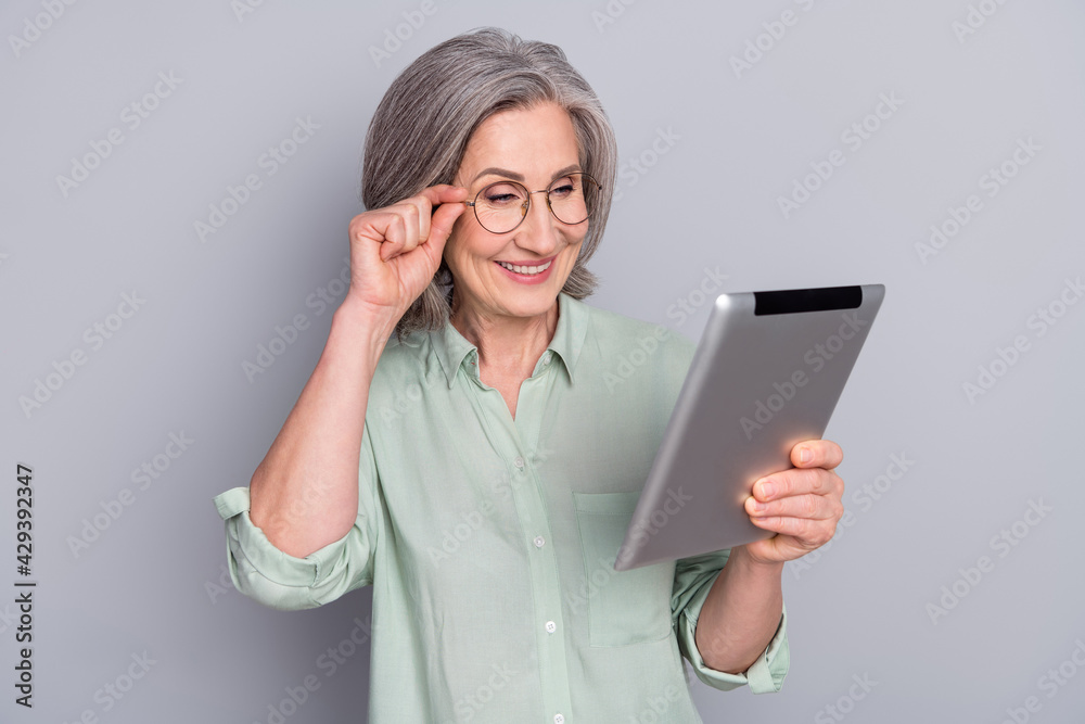 Photo of happy smiling lovely charming mature businesswoman promoter work in tablet isolated on grey color background Photo of happy smiling lovely charming mature businesswoman promoter work in tablet isolated on grey color background