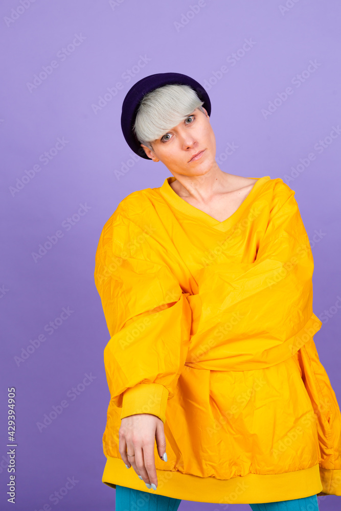 Stylish european woman on purple background posing wearing yellow large jacket and hat Stylish european woman on purple background posing wearing yellow large jacket and hat