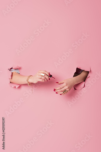 Partial view of woman applying nail polish near pink background with holes