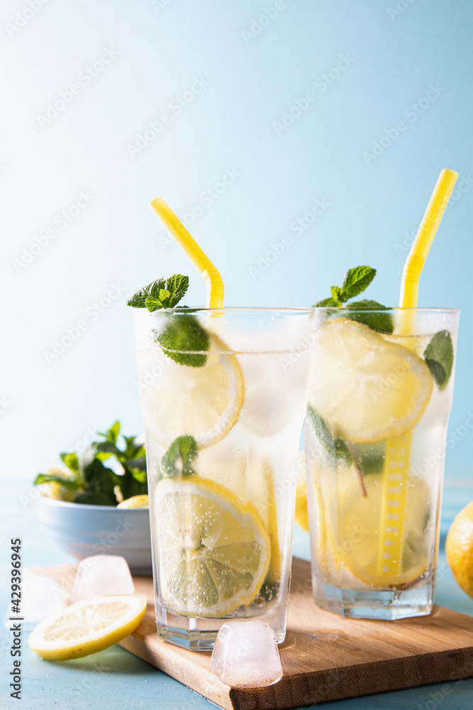 Two glass with lemonade or mojito cocktail with lemon and mint, cold refreshing drink or beverage with ice on blue background. Copy space Two glass with lemonade or mojito cocktail with lemon and mint, cold refreshing drink or beverage with ice on blue background. Copy space