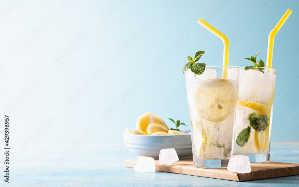 Two glass with lemonade or mojito cocktail with lemon and mint, cold refreshing drink or beverage with ice on blue background. Copy space - obrazy, fototapety, plakaty 