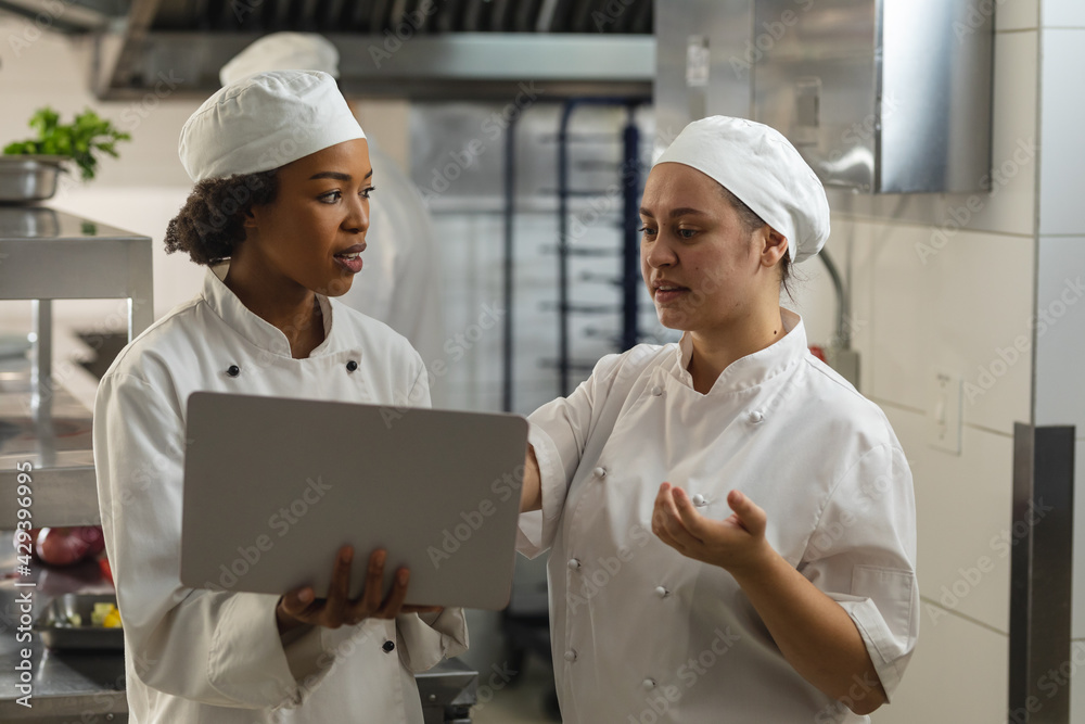 Portrait of diverse race female professional chefs discussig over laptop Portrait of diverse race female professional chefs discussig over laptop