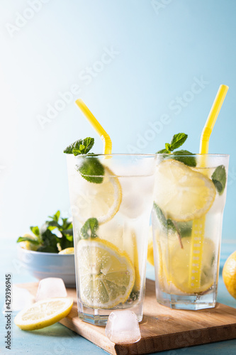 Two glass with lemonade or mojito cocktail with lemon and mint, cold refreshing drink or beverage with ice on blue background. Copy space
