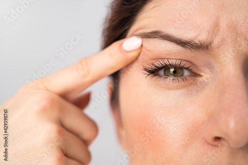 Close-up portrait of Caucasian middle-aged woman pointing to the wrinkles on the upper eyelid. Signs of aging on the face photo
