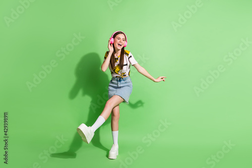 Full length photo of attractive cheerful young woman look empty space dance wear headphones isolated on green color background