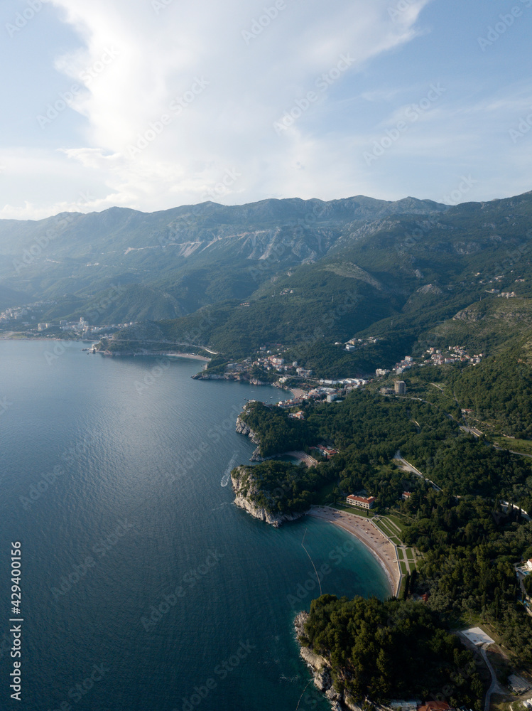 Aerial view of mountainous landscape Adriatic sea coast near Sveti Stefan island. Milocer beach, green sidehill with rich vegetation, trees, forest, coastal small villages, cities. Montenegro nature