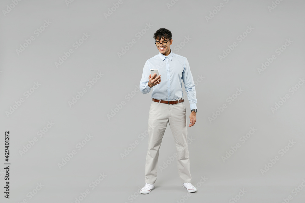 Full length young fun successful employee business latin man corporate lawyer 20s in classic white shirt glasses hold in hand using mobile cell phone isolated on grey color background studio portrait