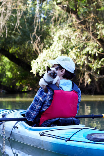 Cat (Mekong bobtail (siames) sits on the shoulder of the woman in blue kayak at the river at summer mrning. Kayaking and travels with pets photo