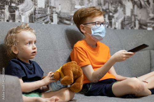 Children watch TV, older brother switches channel, holding the remote control.