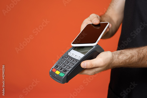 Wallpaper Mural Close up cropped photo shot young man barista barman employee in apron white t-shirt work in coffee shop use wireless bank payment terminal credit payment mobile phone isolated on orange background Torontodigital.ca