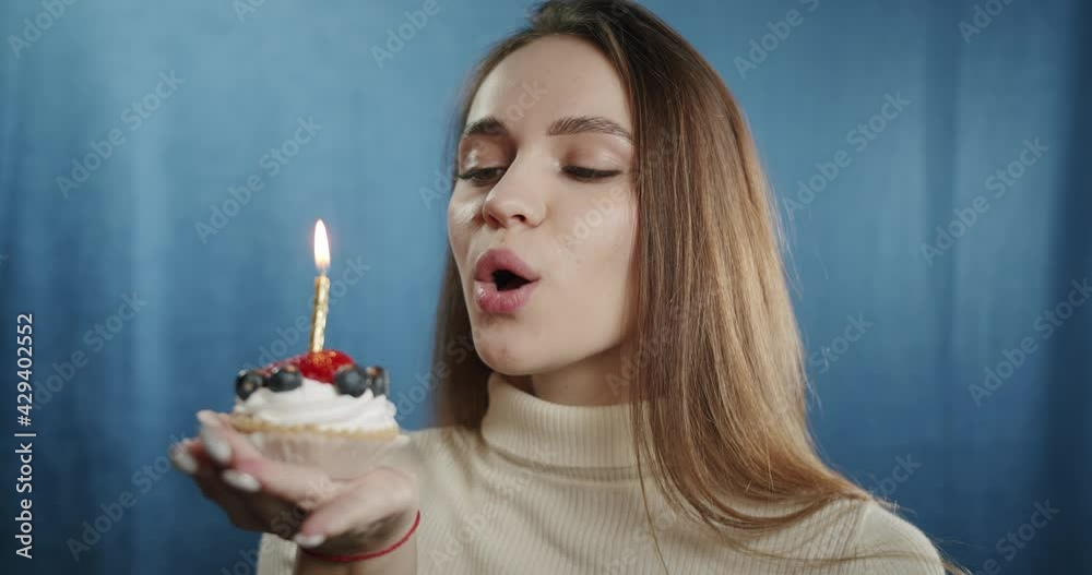 Portrait of young woman blowing out the candle on delicious sweet cake with berries, looking in camera with wide smile. Close-up of female student with green eyes. Happy beautiful model in studio. Portrait of young woman blowing out the candle on delicious sweet cake with berries, looking in camera with wide smile. Close-up of female student with green eyes. Happy beautiful model in studio.