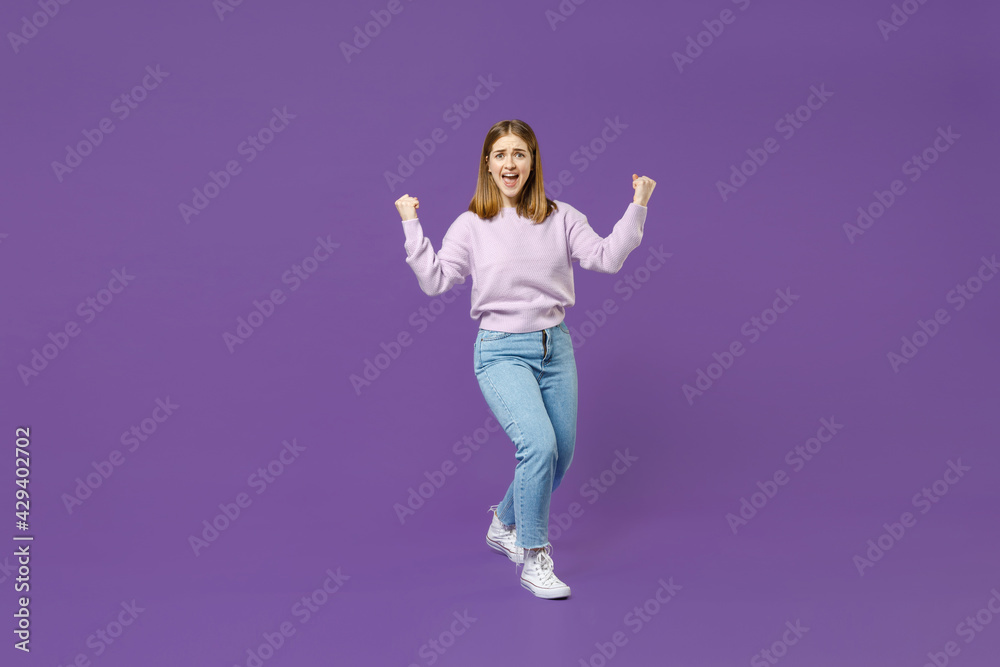 Full length young overjoyed happy fun excited student caucasian woman 20s in purple sweater do winner gesture clench fist with isolated on violet background studio portrait People lifestyle concept.