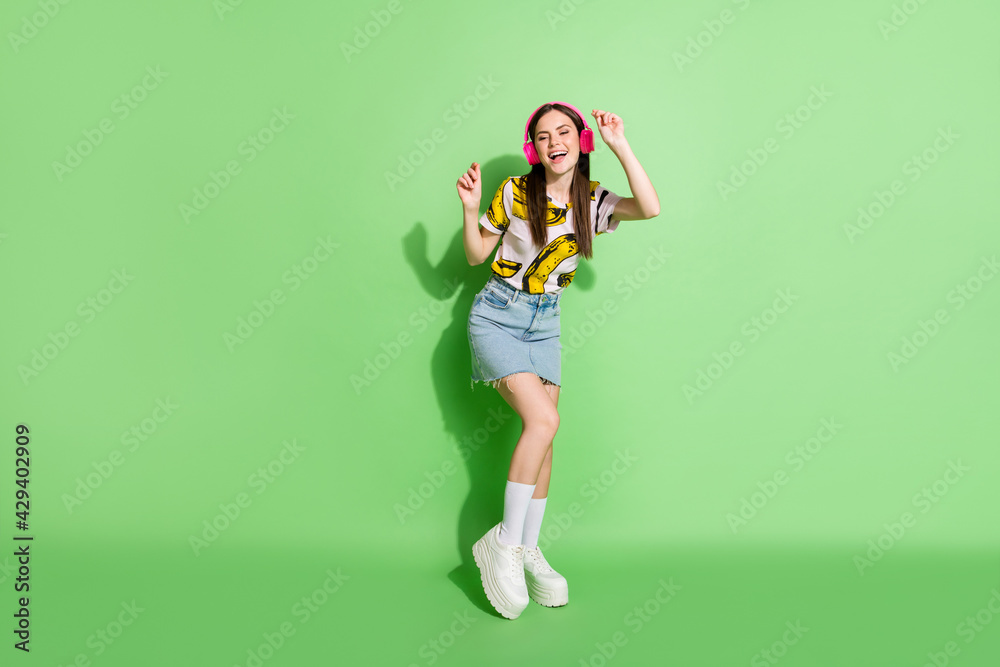 Full size photo of young smiling dreamy charming girl in headphones dancing isolated on green color background Full size photo of young smiling dreamy charming girl in headphones dancing isolated on green color background