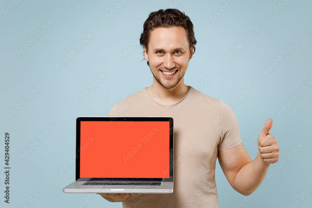 Young smiling caucasian man 20s wear casual basic beige t-shirt hold laptop pc computer with blank screen workspace area show thumb up like gesture isolated on pastel blue background studio portrait Young smiling caucasian man 20s wear casual basic beige t-shirt hold laptop pc computer with blank screen workspace area show thumb up like gesture isolated on pastel blue background studio portrait