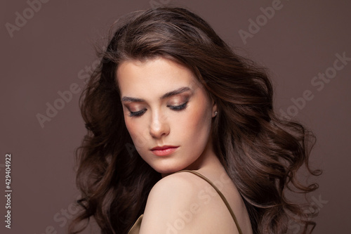 Portrait of lovely woman brunette with clear skin and healthy wavy hairstyle on brown background. Beautiful woman with closed eyes and natural makeup