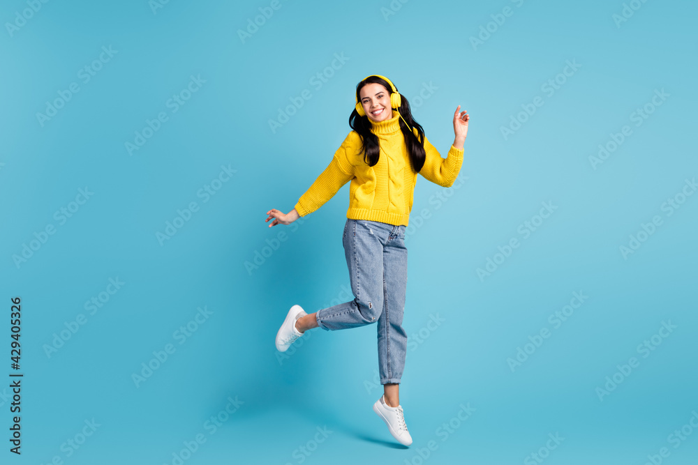 Full length body size side photo of brunette woman jumping dancing listening music in earphones isolated on vivid blue color background Full length body size side photo of brunette woman jumping dancing listening music in earphones isolated on vivid blue color background