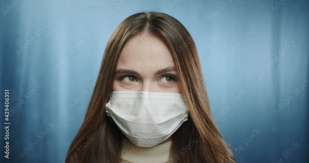 Covid-19, pandemic and quarantine concept. Close-up of serious teenager student woman wearing medical protective mask during coronavirus, standing against blue background. Covid-19, pandemic and quarantine concept. Close-up of serious teenager student woman wearing medical protective mask during coronavirus, standing against blue background.
