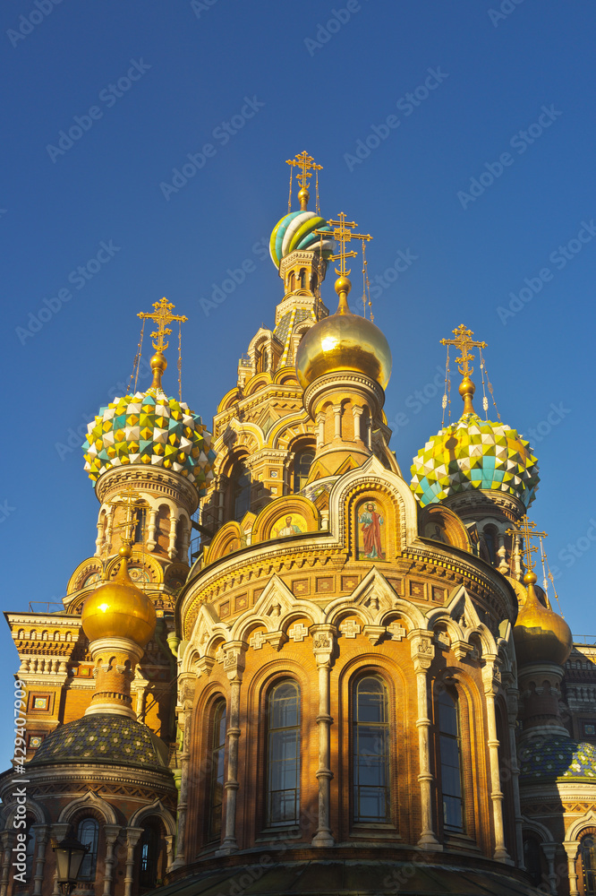 St. Petersburg. Beautiful domes of Cathedral of Savior on Spilled Blood (Spas na Krovi) against the background of a blue sky and ornate exterior with masaic icons on walls of church in sunset light