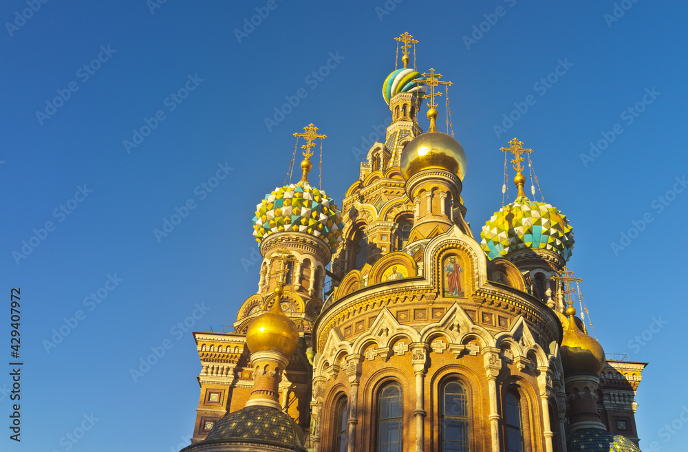 Saint Petersburg. Beautiful domes of the Cathedral of the Savior on Spilled Blood (Spas na Krovi) and ornate exterior with mosaic icons against the background of a blue cloudless sky at sunset