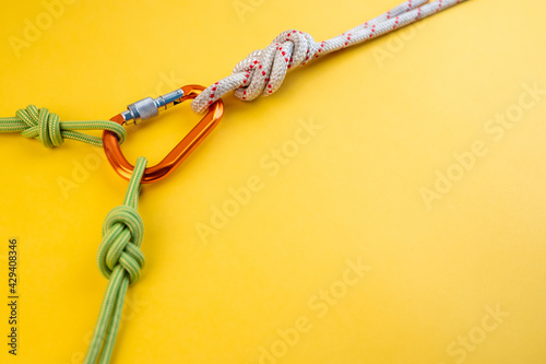 Orange Carabiner with rope. Equipment for climbing and mountaineering, alpinism, rappelling. Safety rope. Knot eight. Isolated on the yellow background. Minimal concept, copy space.
 photo