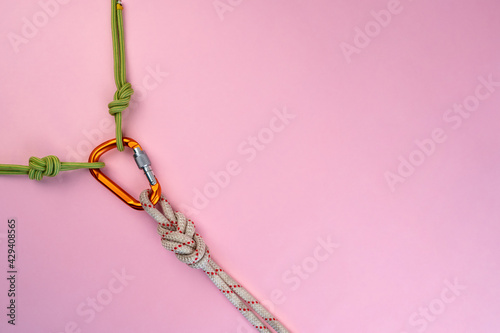 Orange Carabiner with rope. Equipment for climbing and mountaineering, alpinism, rappelling. Safety rope. Knot eight. Isolated on the pink background. Minimal concept, copy space. 
