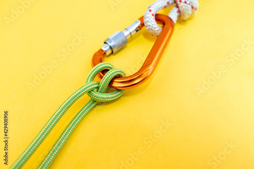Orange carabiner. Equipment for climbing and mountaineering. Safety rope. Knot Prusik, clove hitch. Isolated on yellow background. 