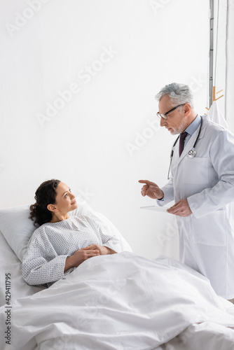 doctor with digital tablet talking to smiling african american woman in hospital