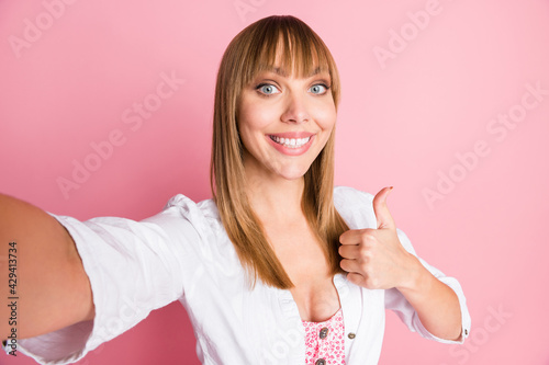 Photo portrait female blogger taking selfie showing thumb-up sign like gesture isolated on pastel pink color background © deagreez