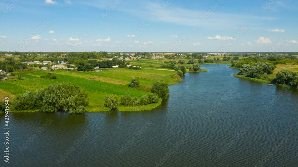 A river in the countryside surrounded by fields of green grass and farmland. Rural landscape in summer.