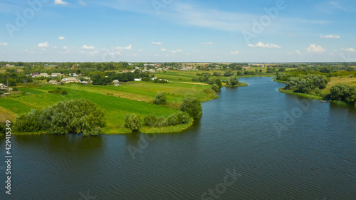 A river in the countryside surrounded by fields of green grass and farmland. Rural landscape in summer.