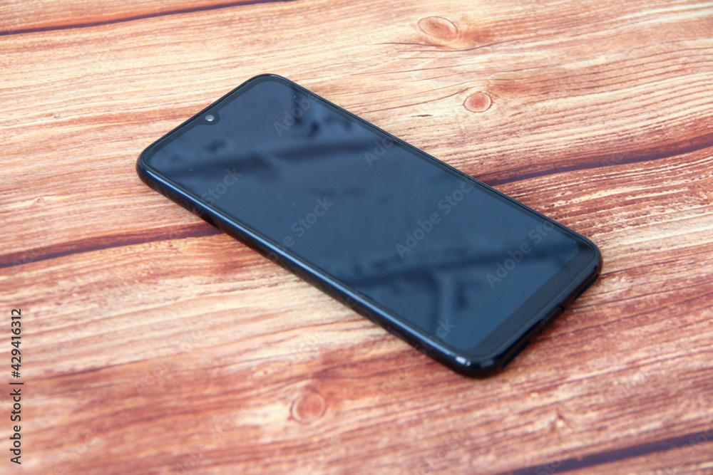 Smartphone with a black screen in which a brick wall is reflected on the wooden background Smartphone with a black screen in which a brick wall is reflected on the wooden background