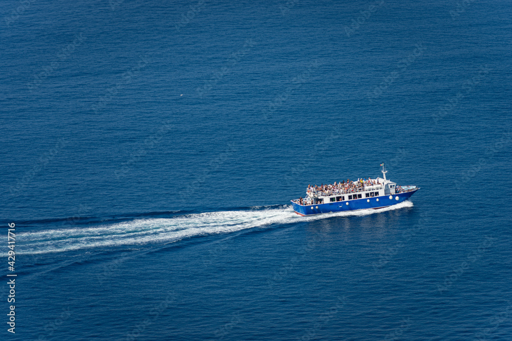 Aerial view of a blue ferry boat with many tourists on board, during sailing to the Cinque Terre in the Mediterranean Sea. Gulf of La Spezia, Liguria, Italy, Europe.