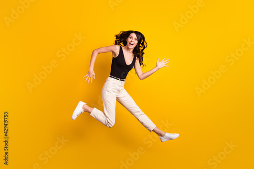 Full length body size photo of girl funny jumping up laughing in casual clothes isolated on vivid yellow color background