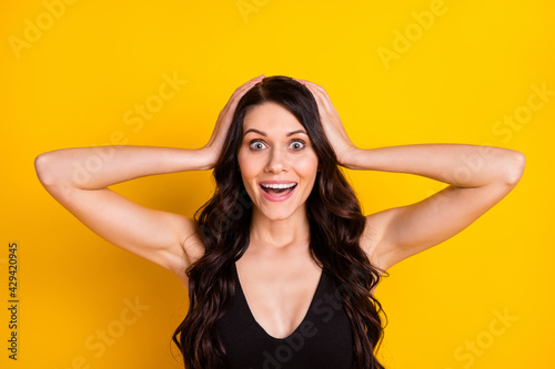 Photo of young excited girl happy positive smile amazed surprised sale news hands touch head isolated over yellow color background