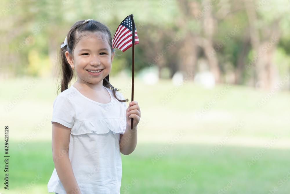 Portrait of little Caucasian girl playing and holding small America flag in her hand at green park. kid celebrate holiday at 4th of July. American Independence Day Portrait of little Caucasian girl playing and holding small America flag in her hand at green park. kid celebrate holiday at 4th of July. American Independence Day