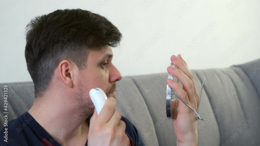 Man is shaving hairs on his face using electric epilator plucking hair