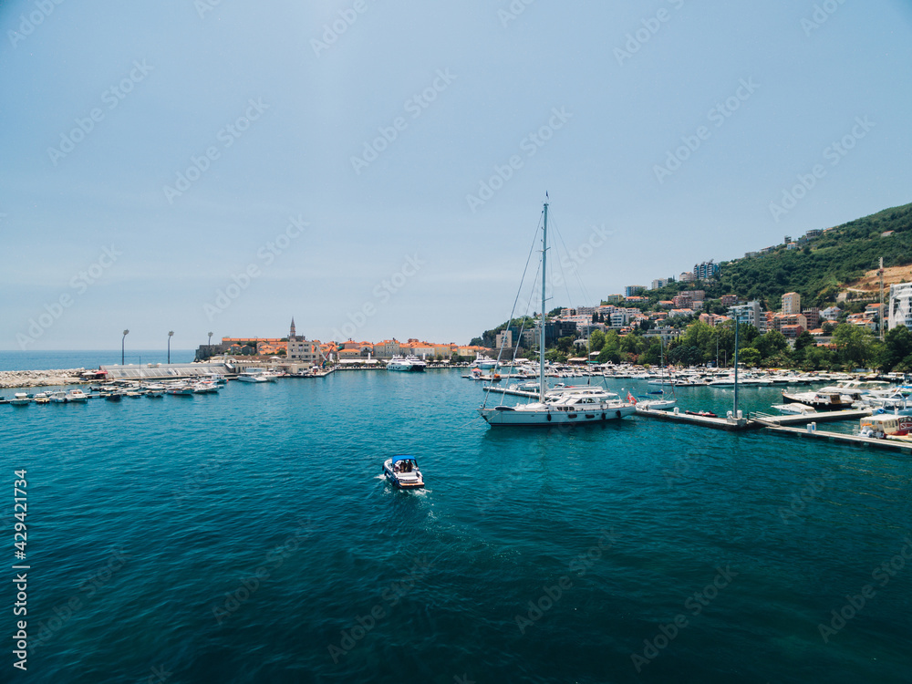 White motor boat sails past the pier of the city of Budva Montenegro on the background of ancient buildings