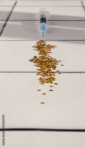 A blurred syringe with a ndle shooting out golden star glitter on a white and black tile background in a hospital. Creative Coronavirus COVID-19 vaccine.. Epidemic virus outbreak concept. photo